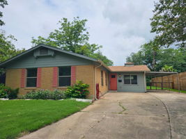 A charming brick exterior with vibrant red shutters, an inviting front door, carport and concrete driveway.
