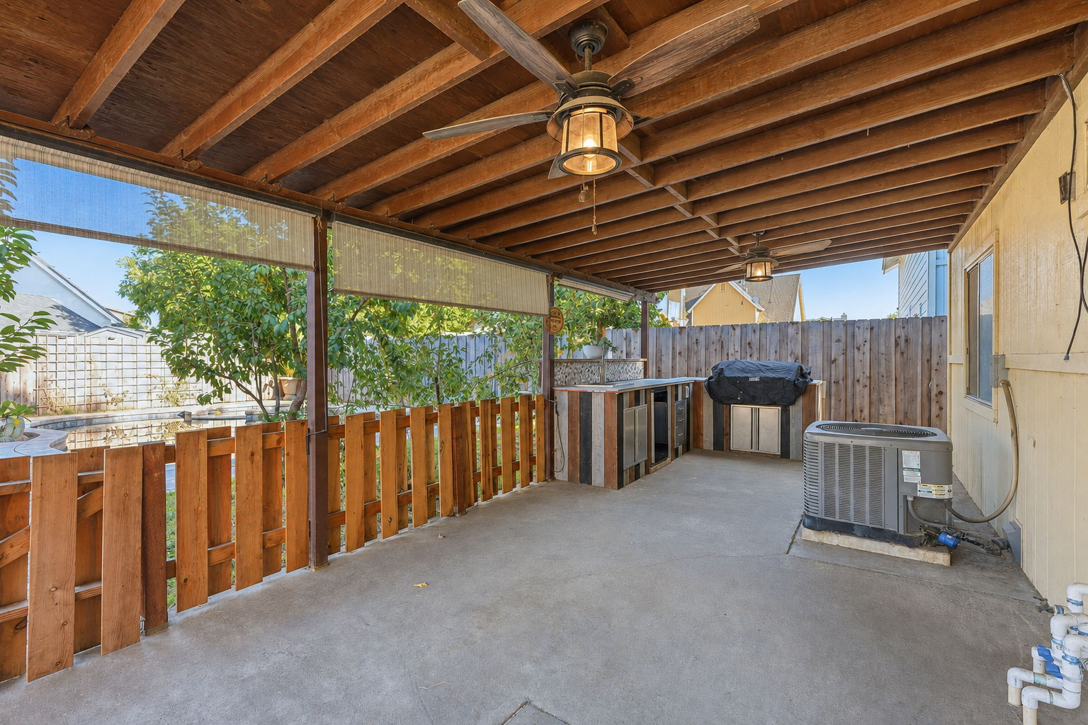 Covered backyard patio with outdoor kitchen, grill, and ceiling fans