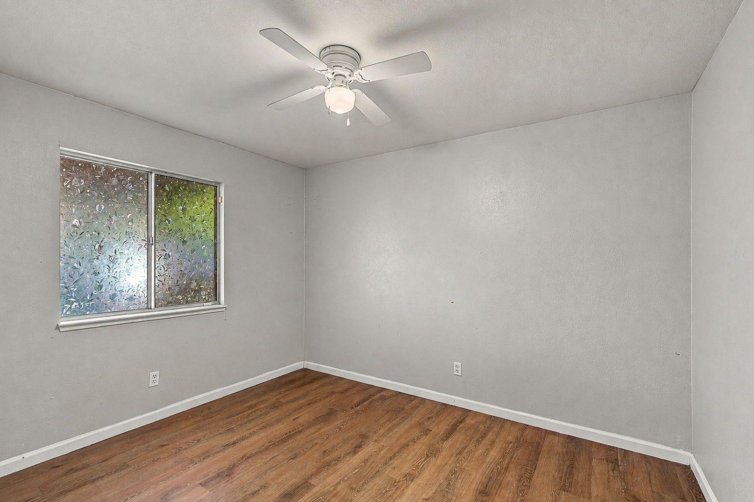 Downstairs bedroom with wood-look flooring and ceiling fan