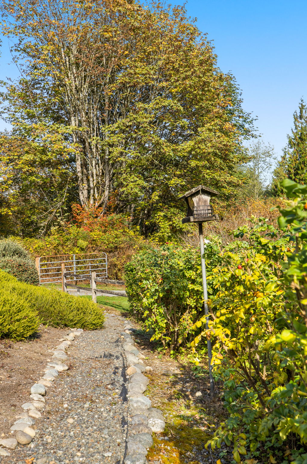 A stone-lined path winds through the garden, with a gate visible in the distance that can be closed to limit access to the property.