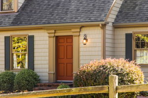 Brick steps lead to a warm wood door, where a glowing lantern light fixture offers guests a cheerful welcome.