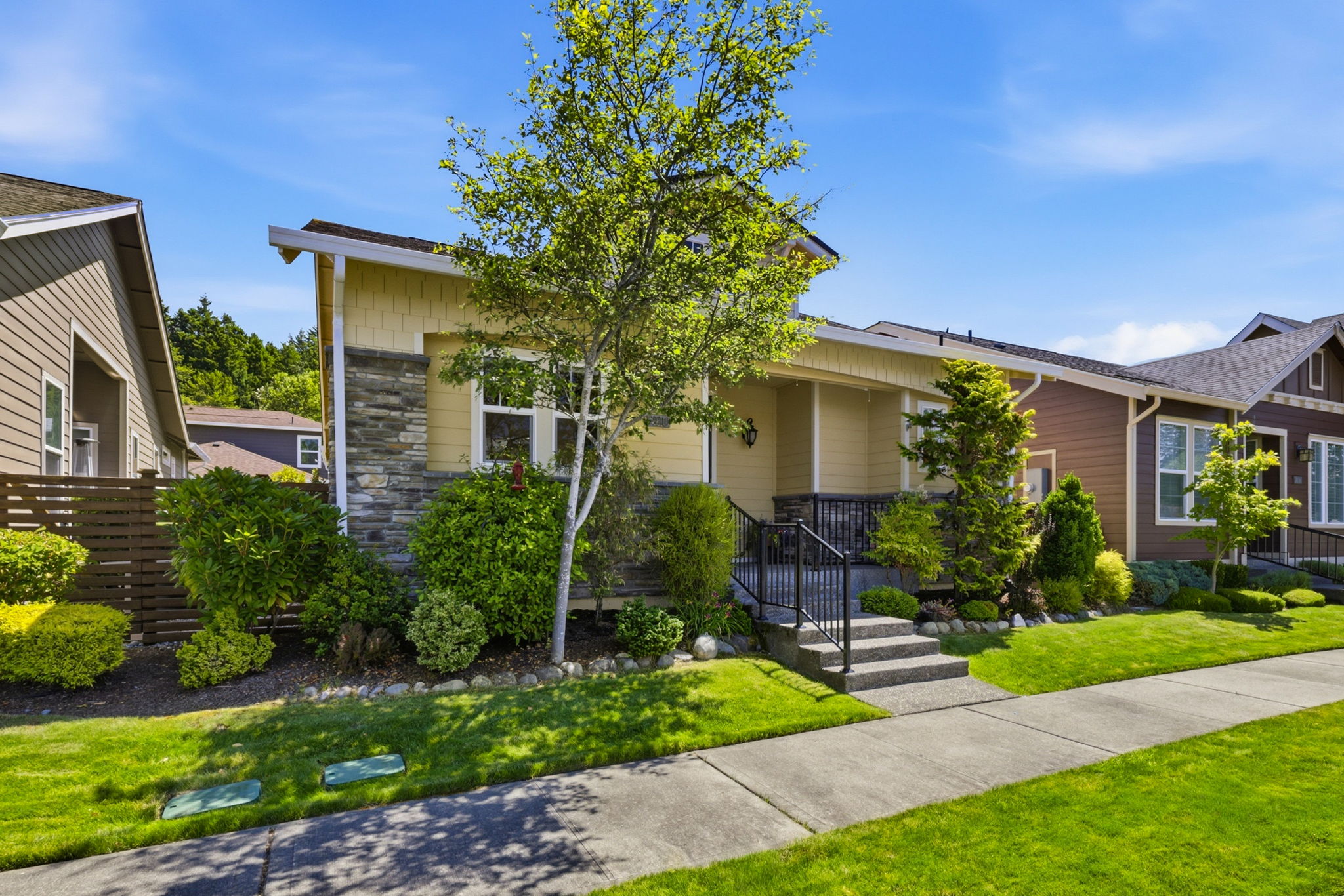 Front Exterior. A tree-lined walkway leads to the covered porch, framed by manicured shrubs and vibrant greenery.