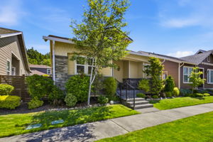 Front Exterior. A tree-lined walkway leads to the covered porch, framed by manicured shrubs and vibrant greenery.