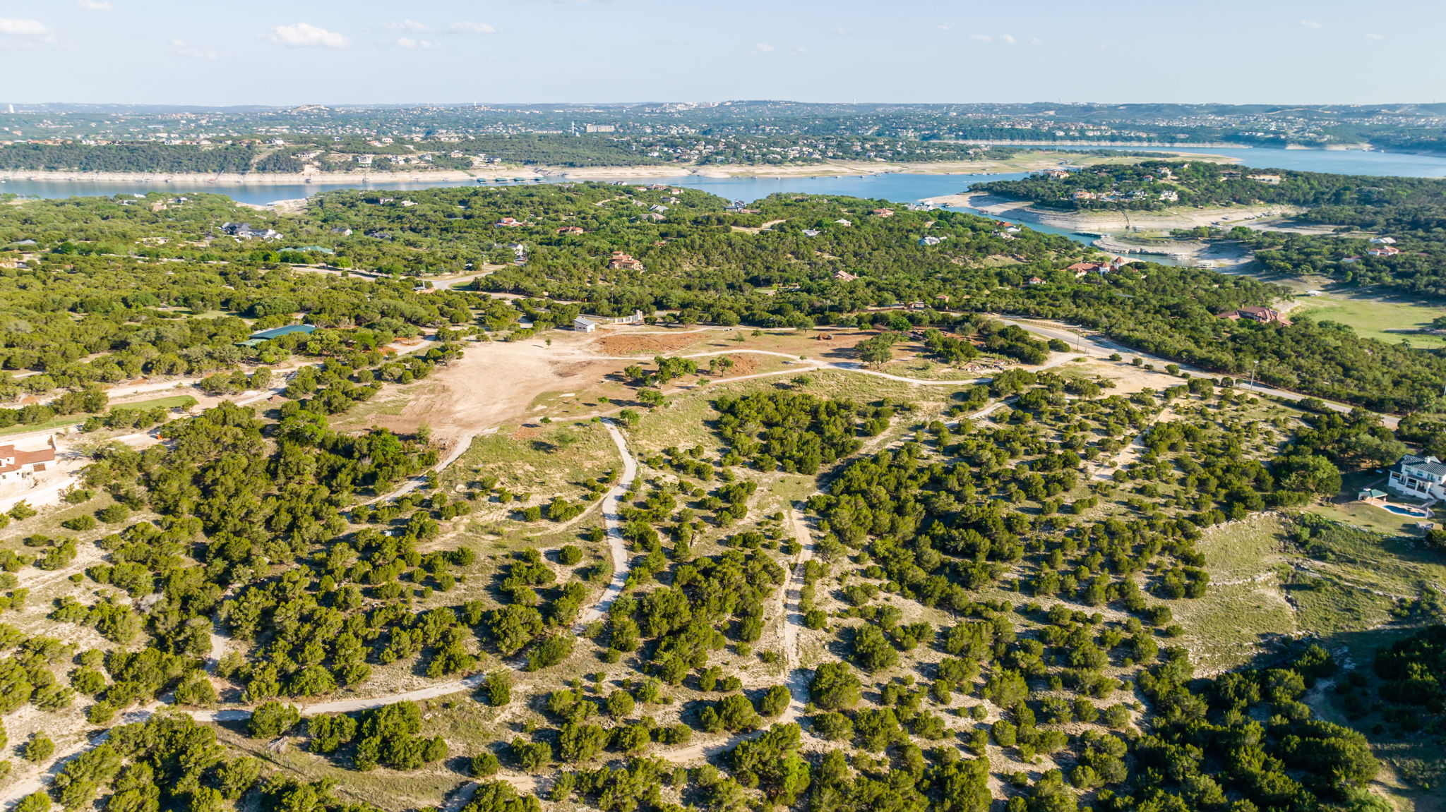 Aerial View shows partially cleared area of the acreage property with Lake Travis in the background and a glimpse of the Coves to the right.