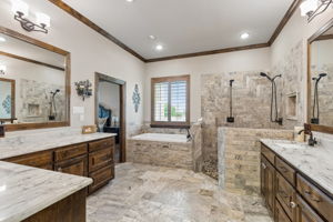 Spa-like ensuite bathroom with oversized soaking tub, stacked stone accents, dual shower heads and vanities.