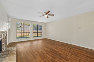 Expansive family room with fireplace and ceiling fan, filled with natural light from large windows that beautifully showcase the room’s scale and design.