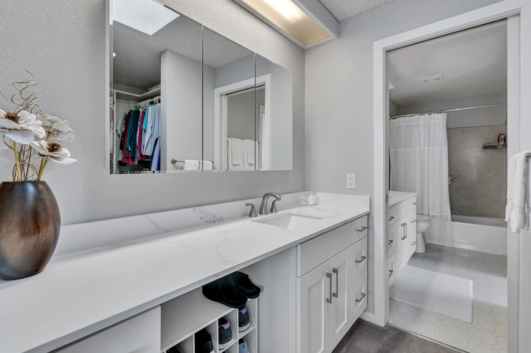 Skylit dressing area off the primary with a sink, mirrored vanity, storage, and walk-in closet.