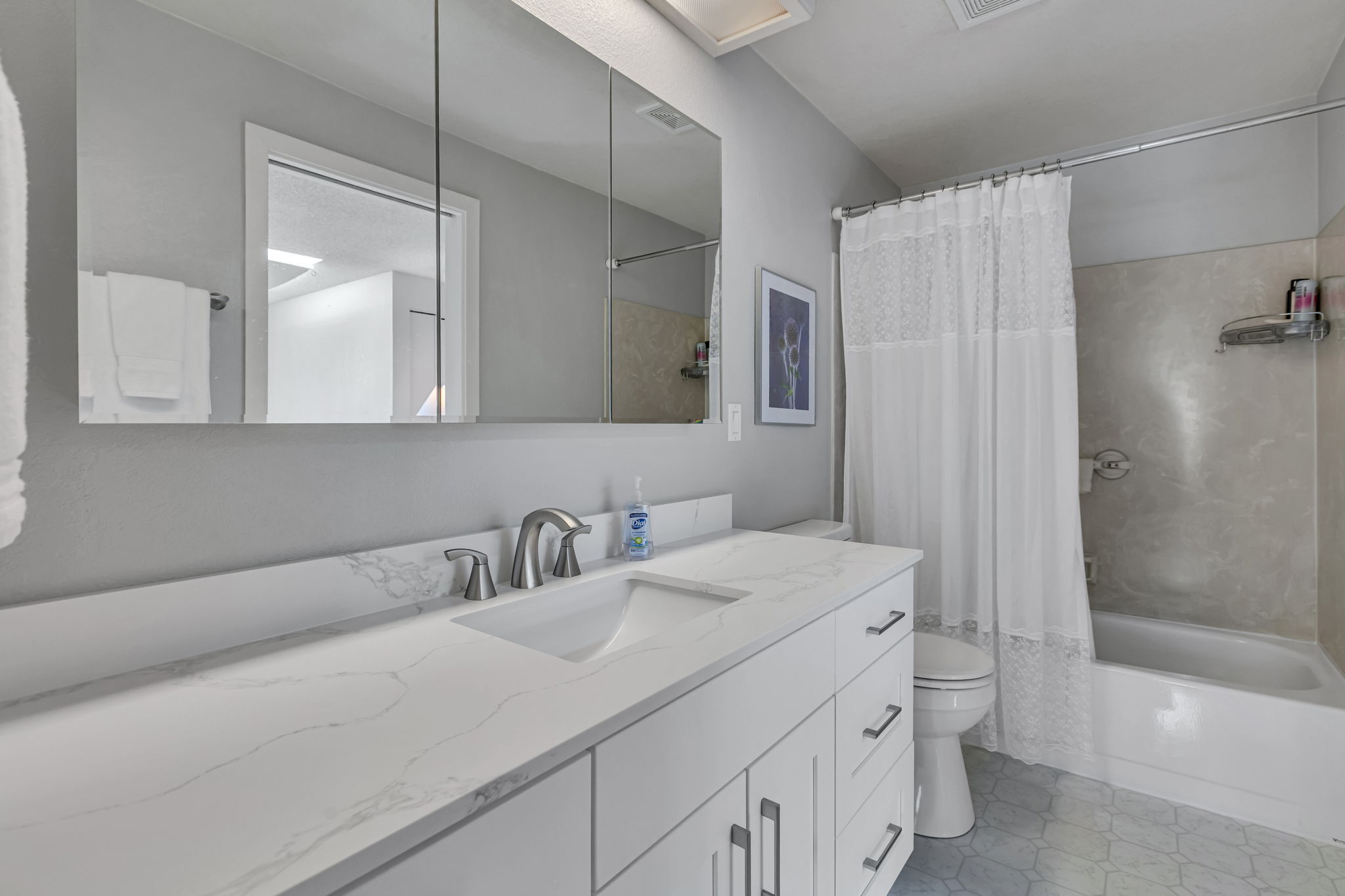 Updated full bath with quartz counters and a large mirrored medicine cabinet.
