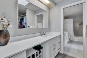 Skylit dressing area off the primary with a sink, mirrored vanity, storage, and walk-in closet.