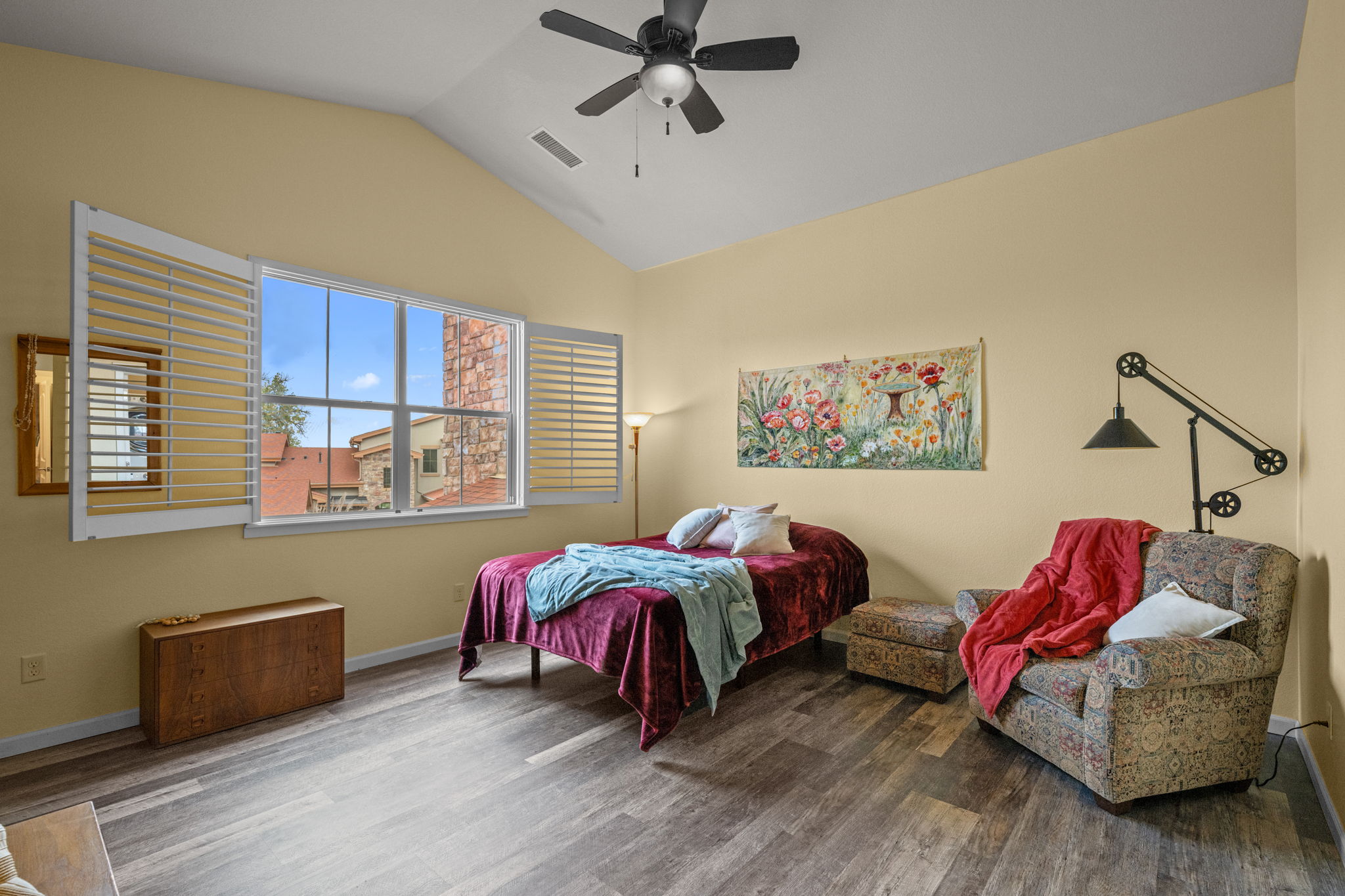 Cheerful primary bedroom with views out large window, plantation shutters, ceiling fan