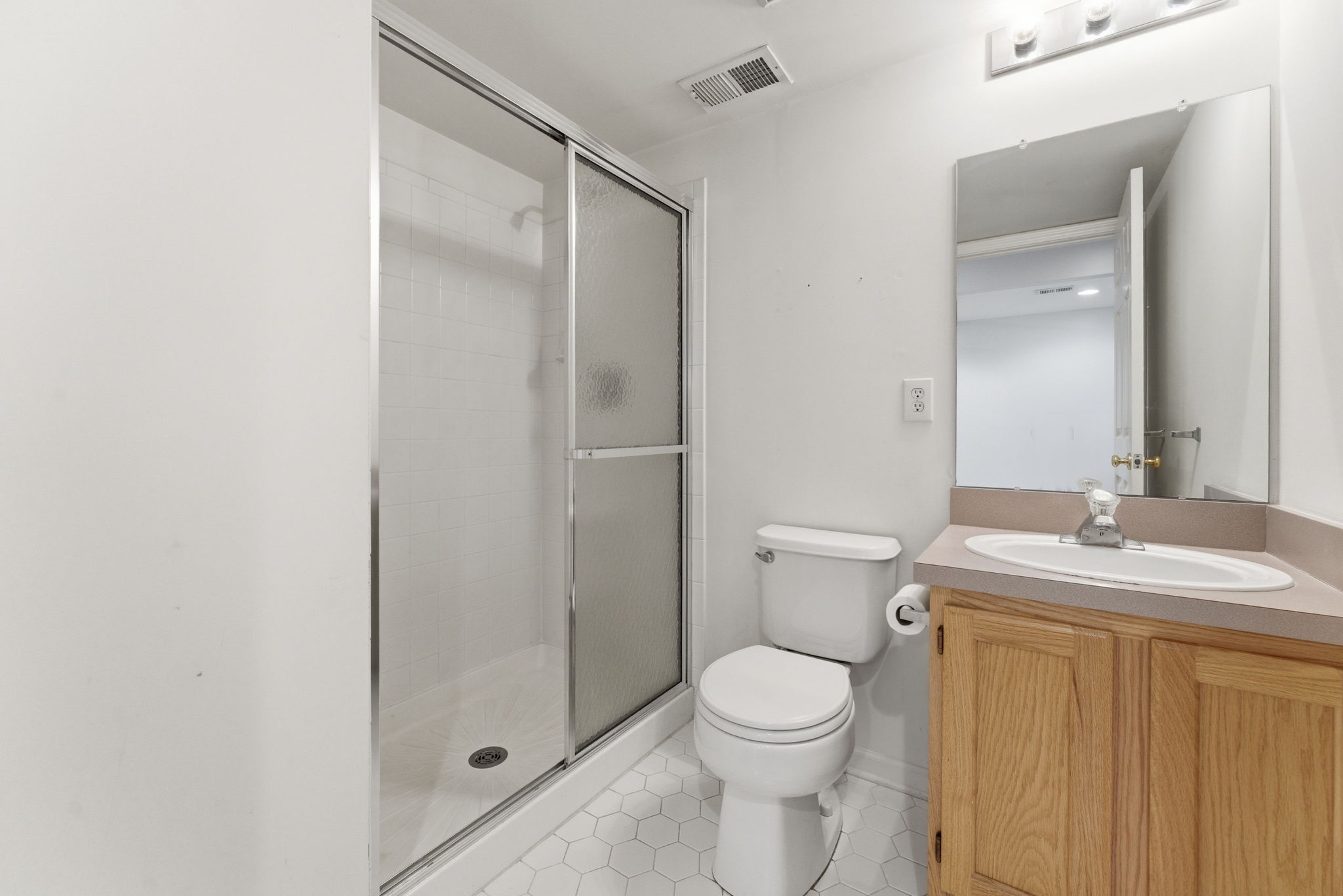 Oak vanity, shower with privacy glass, ceramic tile floor.