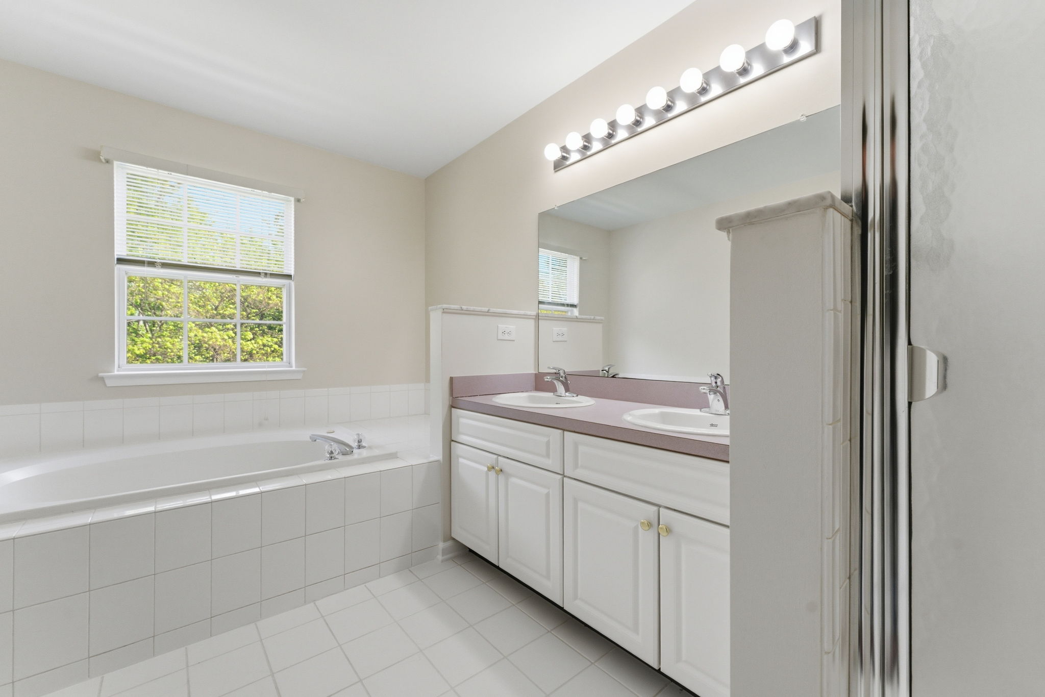 Double basins in a white vanity, a jetted soaking tub in tile surround and large shower in tile surround with privacy glass.