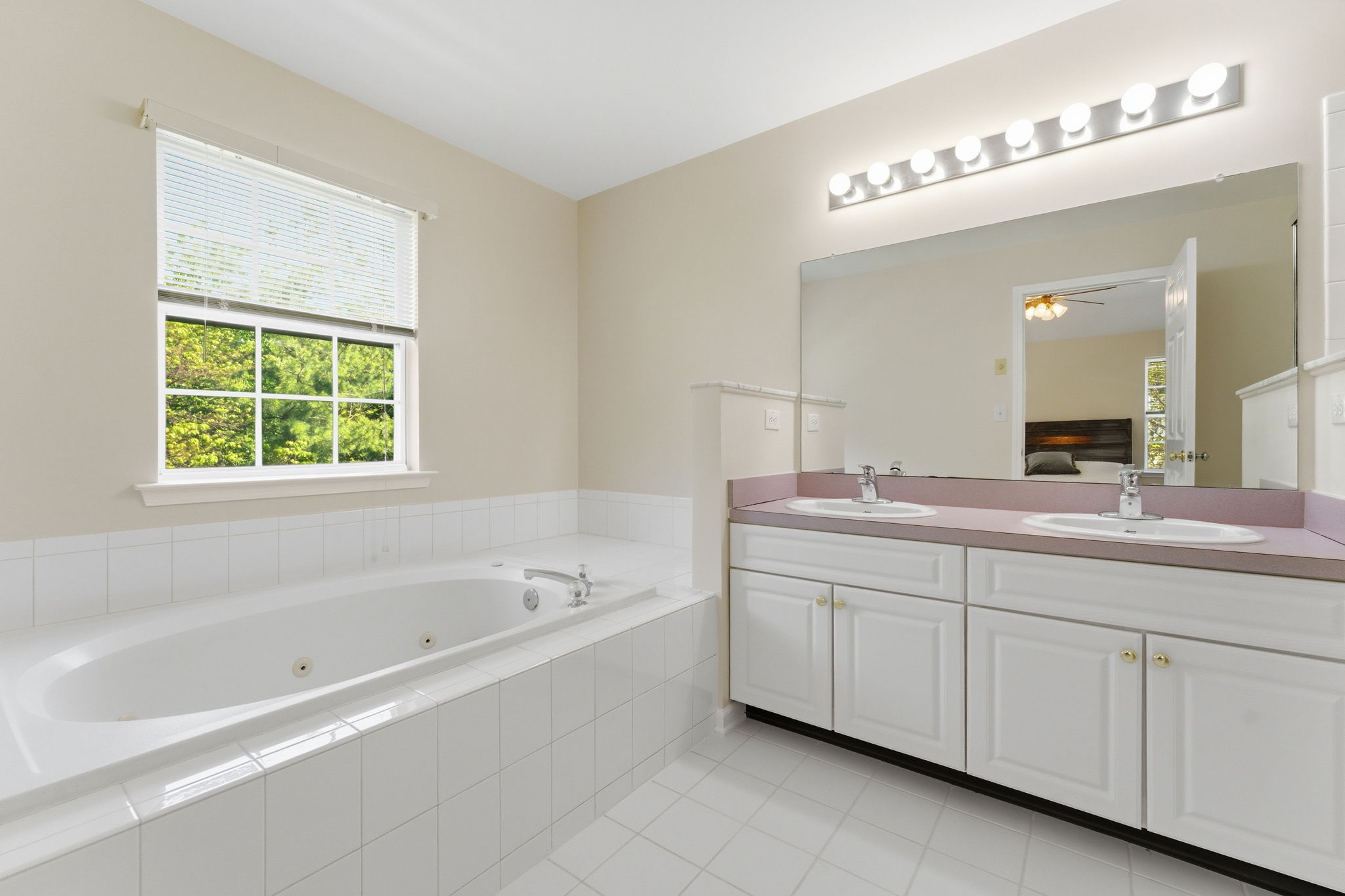Double basins in a white vanity, a jetted soaking tub in tile surround and large shower in tile surround with privacy glass.