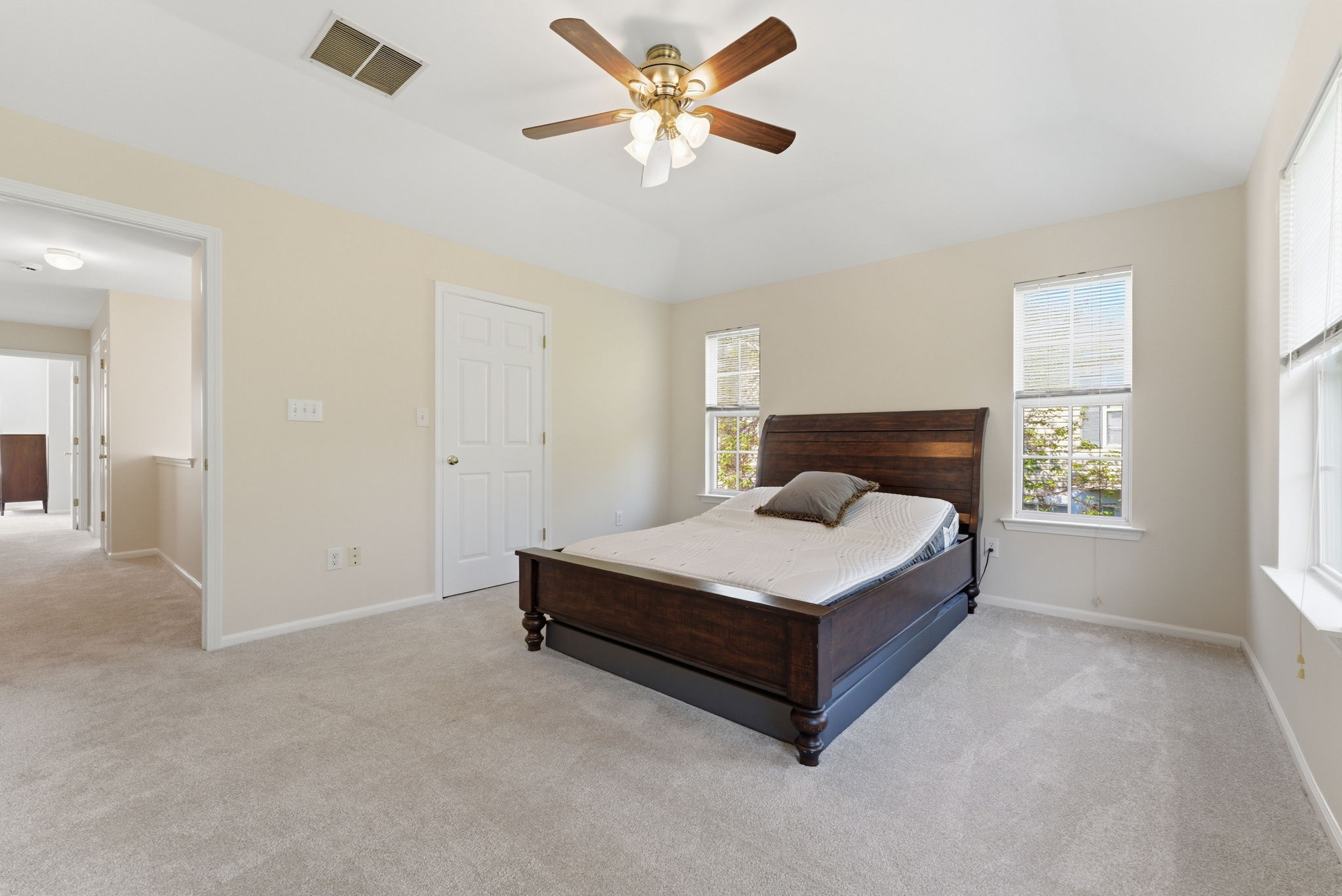 Spacious primary suite features a deep tray ceiling, ceiling fan, a large walk-in closet and newer wall-to-wall carpet.