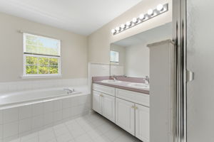 Double basins in a white vanity, a jetted soaking tub in tile surround and large shower in tile surround with privacy glass.