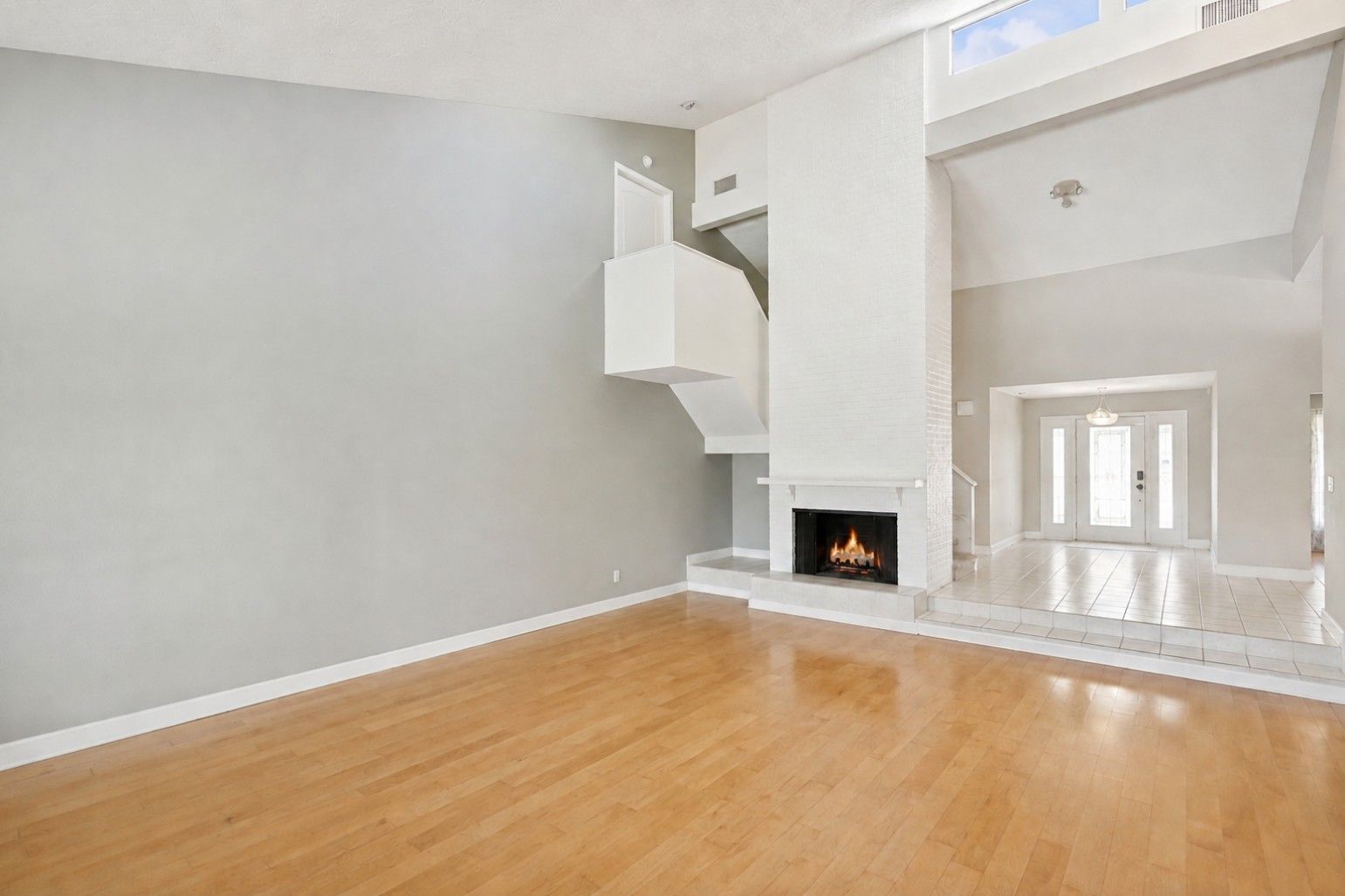 Inviting foyer and family room featuring a floor-to-ceiling brick fireplace, skylights that fill the space with natural light, and a staircase leading to three spacious upstairs bedrooms.