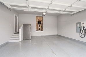 Spacious attached 2-car garage featuring tall ceilings, epoxy-coated floors, Tesla EV charger, and additional storage space.