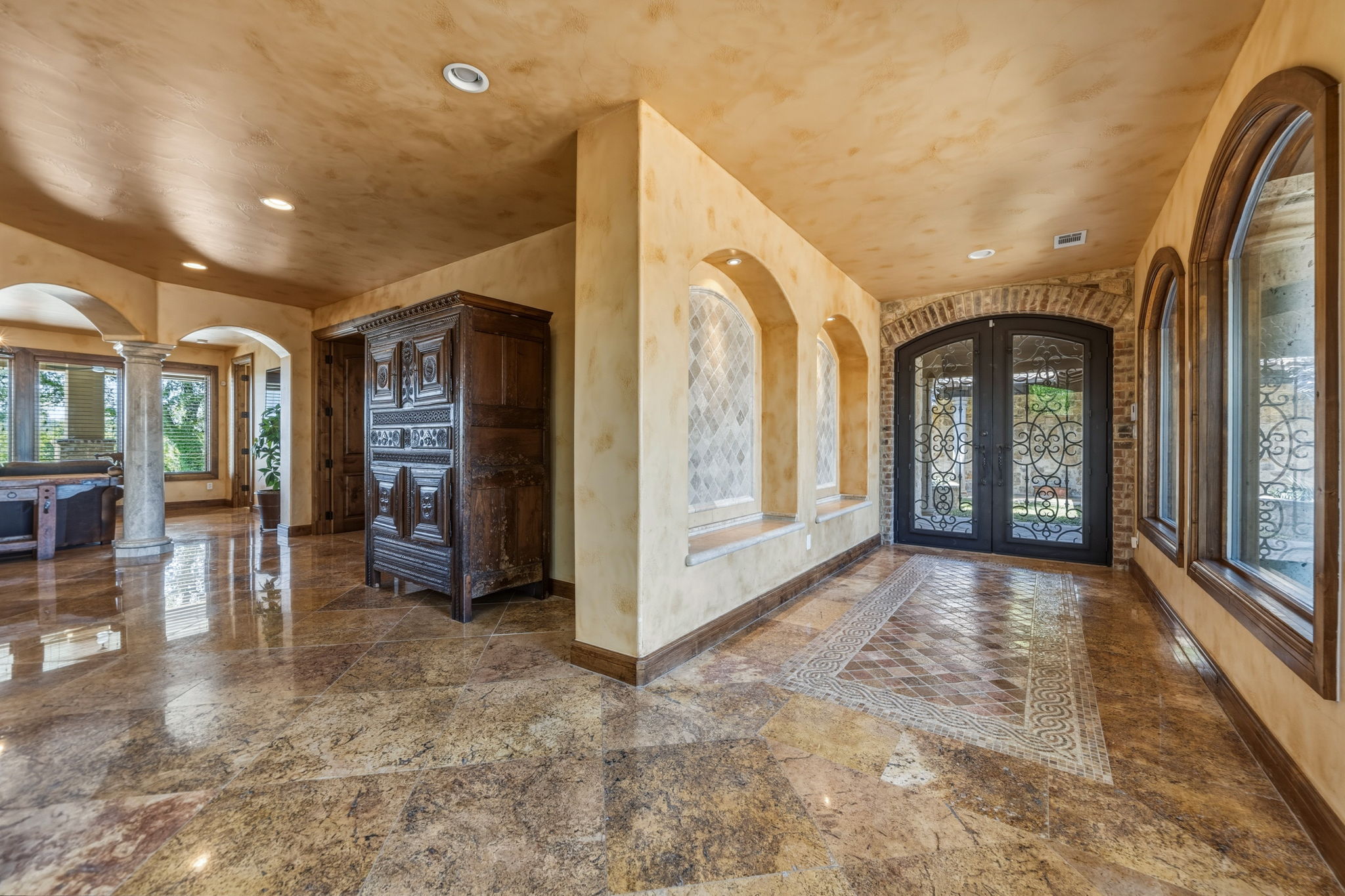 Spacious interior hallway featuring polished stone flooring, arched doorways, and recessed lighting.