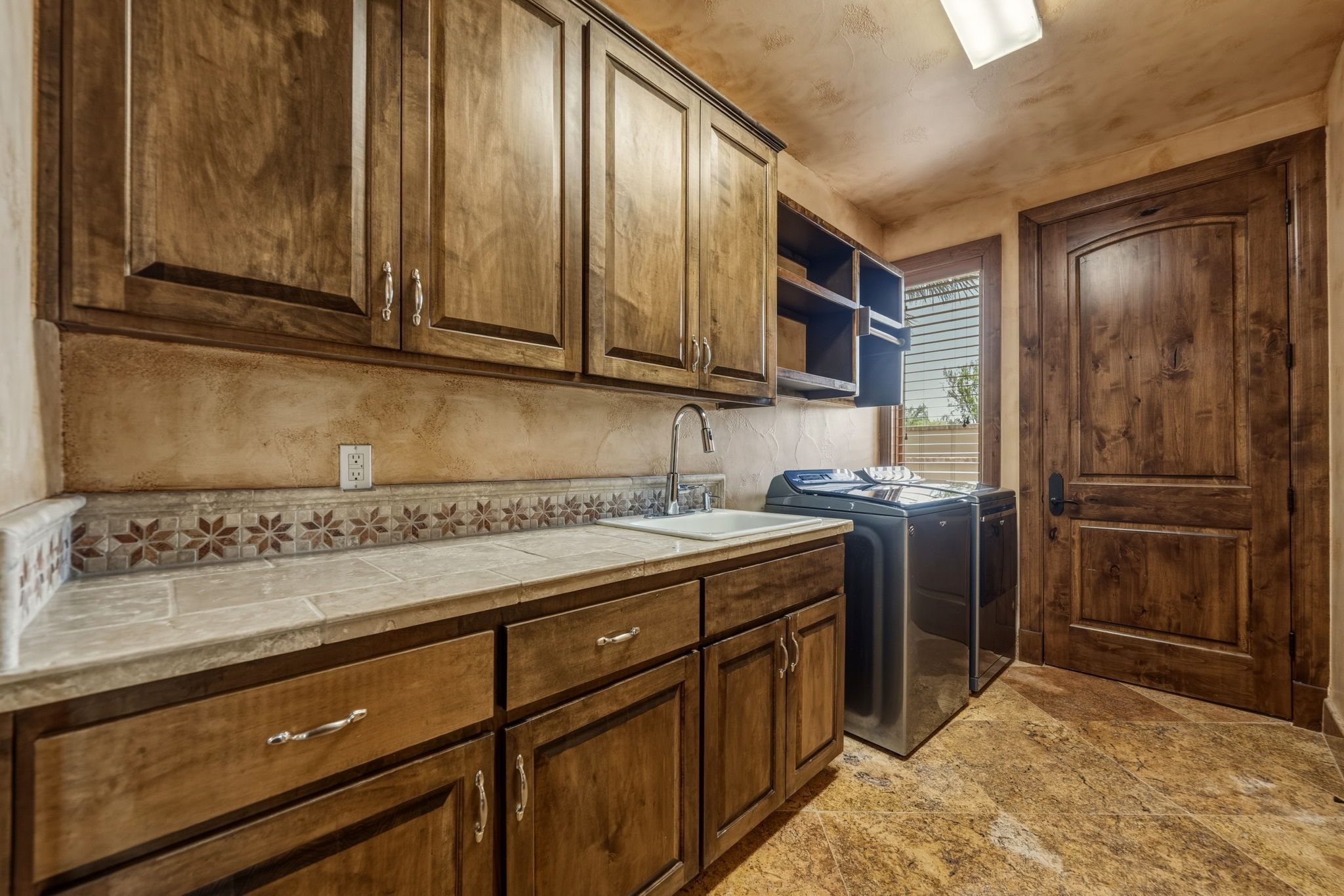 Laundry room consists of a large sink, knotty alder cabinetry and a washer and dryer.