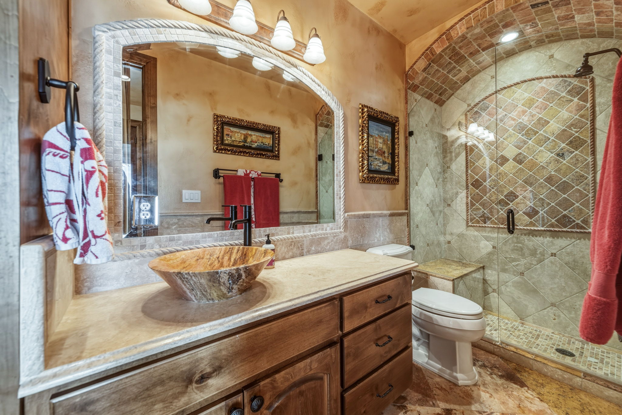 Lower level bathroom featuring a wooden vanity with a stone countertop, a unique natural stone vessel sink, and an arched mirror.