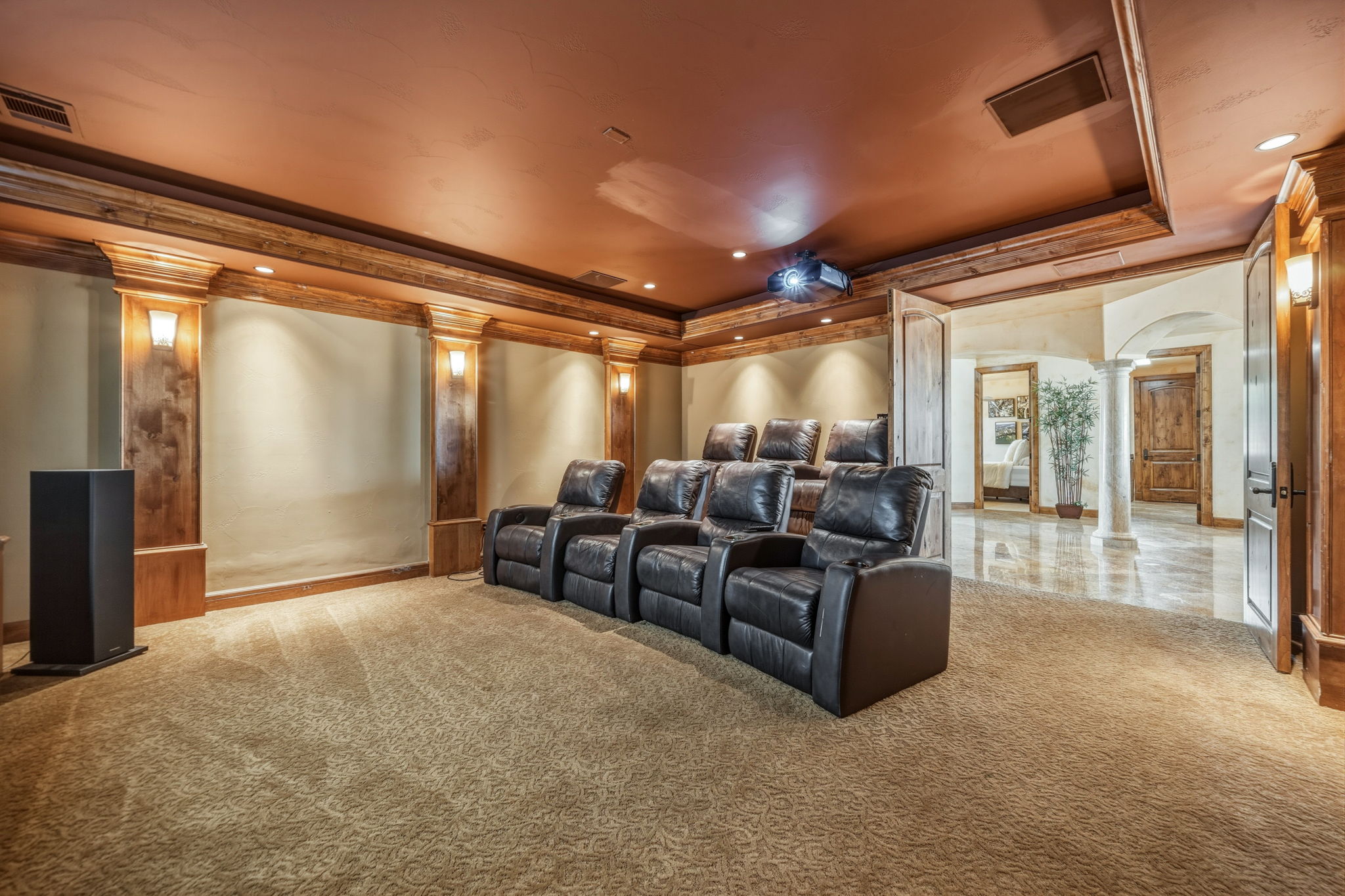 Home theater features a projector, a large screen, and rows of brown leather recliners.  You can see the downstairs living area outside the doors.