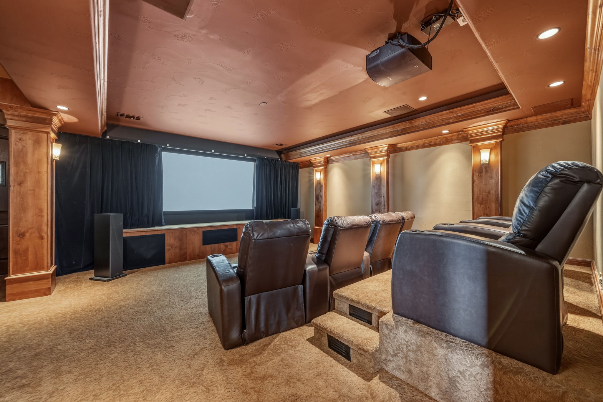 Experience cinematic comfort in the dedicated home theater room, featuring tiered seating with leather recliners, a large projection screen, and a ceiling-mounted projector.