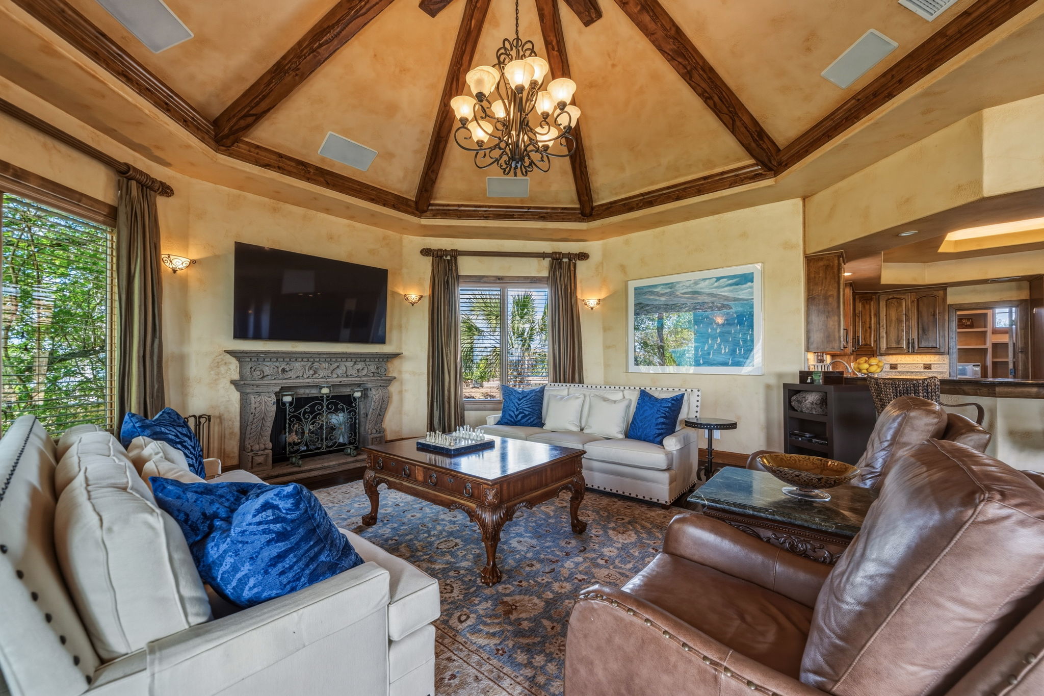 The living area features a high vaulted ceiling with exposed wooden beams, hand-carved stone fireplace, and surround sound speakers.