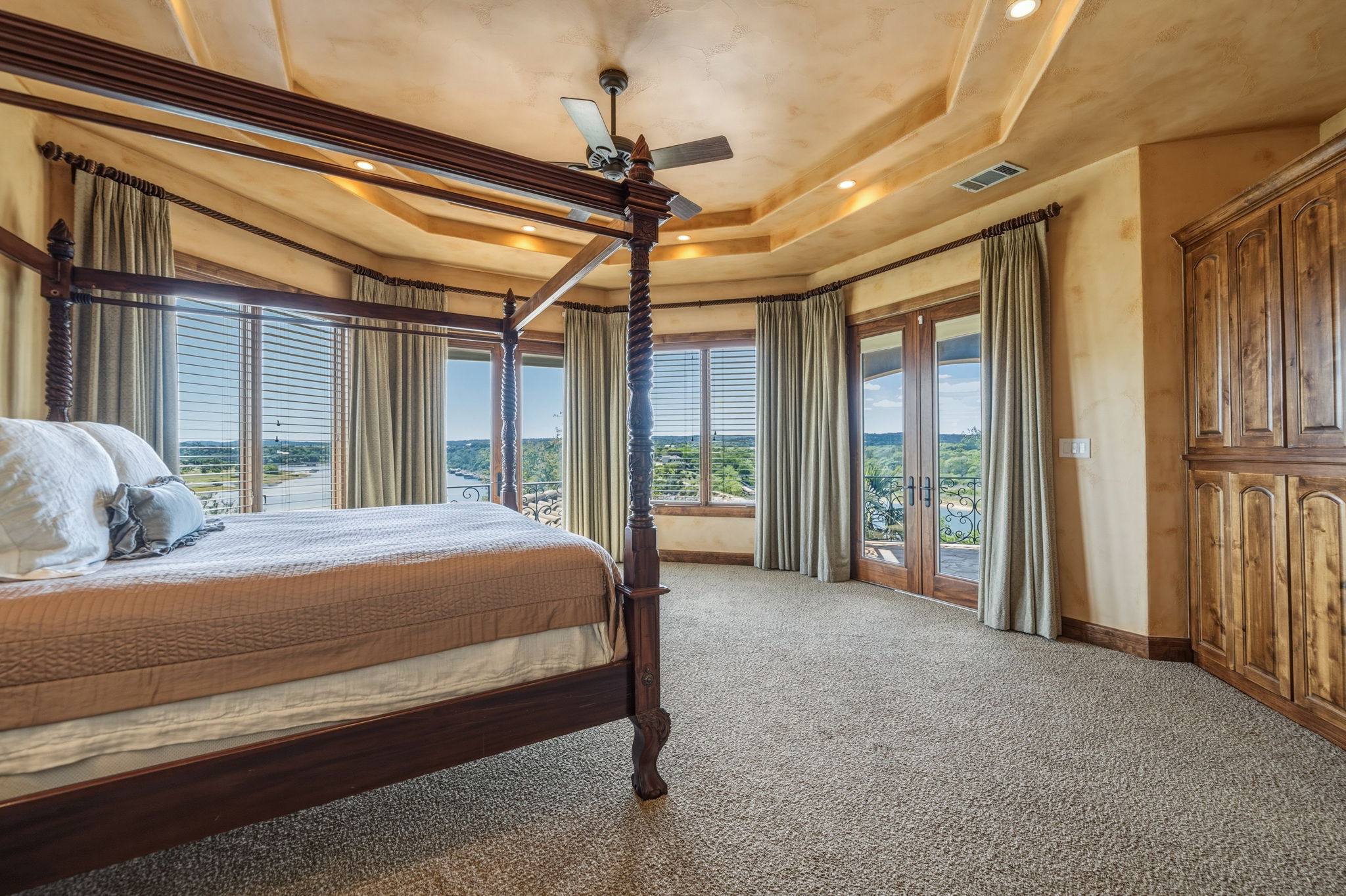 Incredible views from the Primary Bedroom.  French doors open to a balcony and the other french doors open to the upper porch.  It features large windows with blinds and drapes, a ceiling fan, and built-in knotty alder cabinetry.