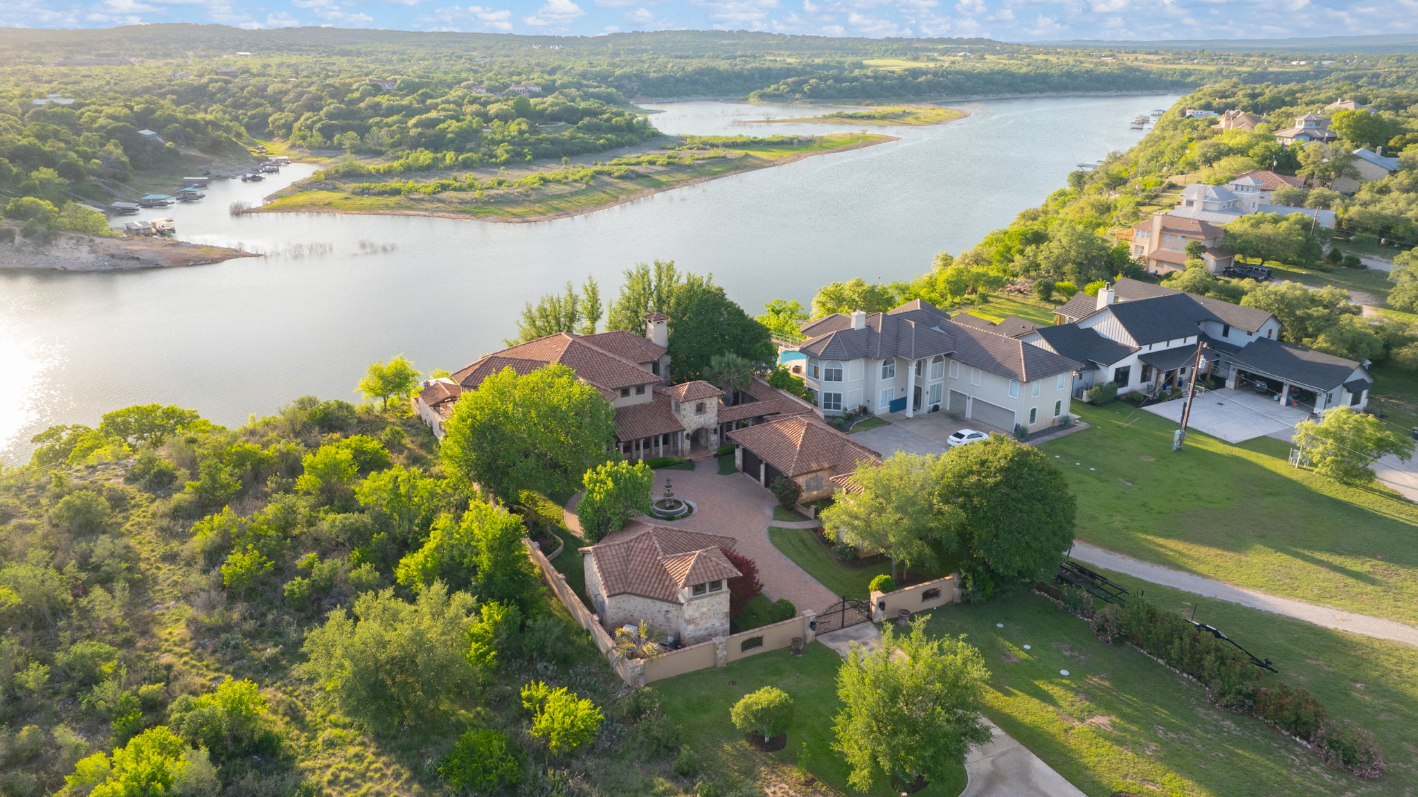 Waterfront views from this Estate home features a gated entrance and a central fountain, set against a backdrop of the hill country.