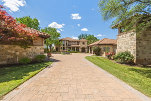 Inside the gate is a circular driveway with a central tiered fountain.  Two detached two-car garages which are insulated and dedicated HVAC with arched wooden doors and a stone facade .