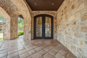 Beautiful Entrance to your home with wrought iron doors, stone walls, brick archways, terracotta floor tiles, and a dark wood ceiling with recessed lighting.