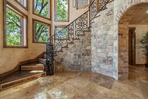 The elegant staircase features ornate wrought iron railings, stone wall accents, and an arched entryway.
