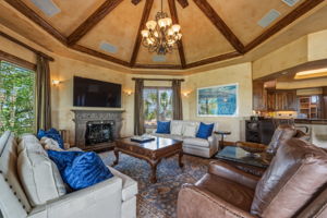 The living area features a high vaulted ceiling with exposed wooden beams, hand-carved stone fireplace, and surround sound speakers.