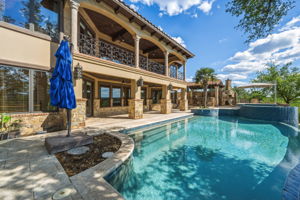 Exterior view features an expansive swimming pool, a second-story balcony with decorative ironwork, and a stone-clad patio area.