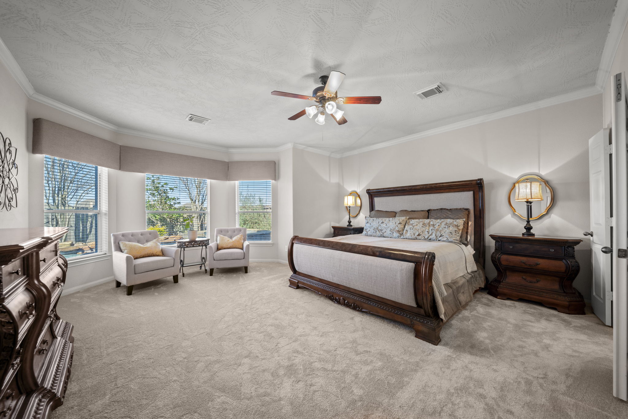 The primary bedroom located downstairs with new carpet (2024), crown molding, a seating area and a stunning view of the pool/spa!