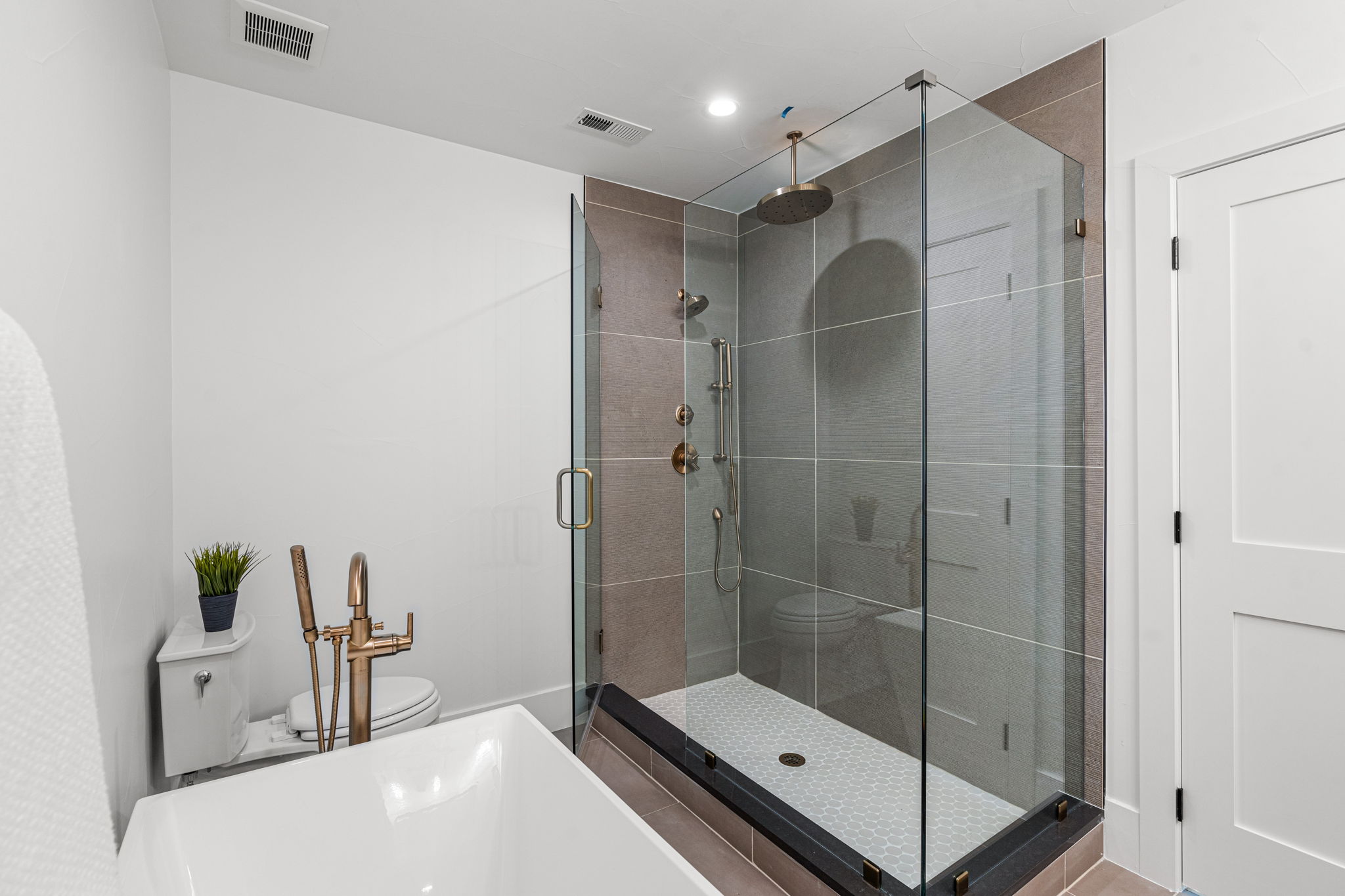 The spacious walk-in shower featuring a glass surround, large rain head, and handheld shower head