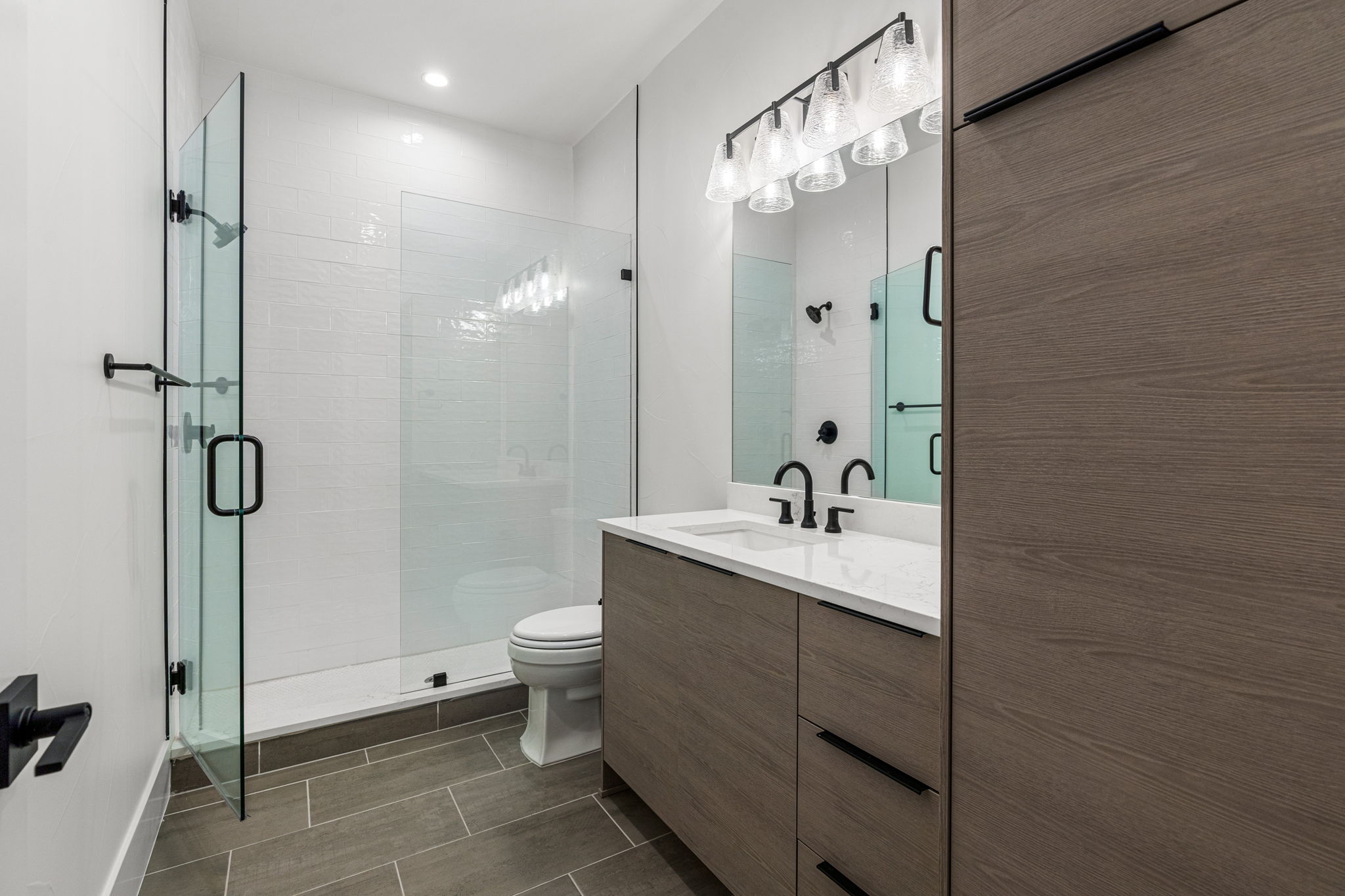 The fourth bathroom has a frameless shower door, decorative tile, & matte black fixtures.