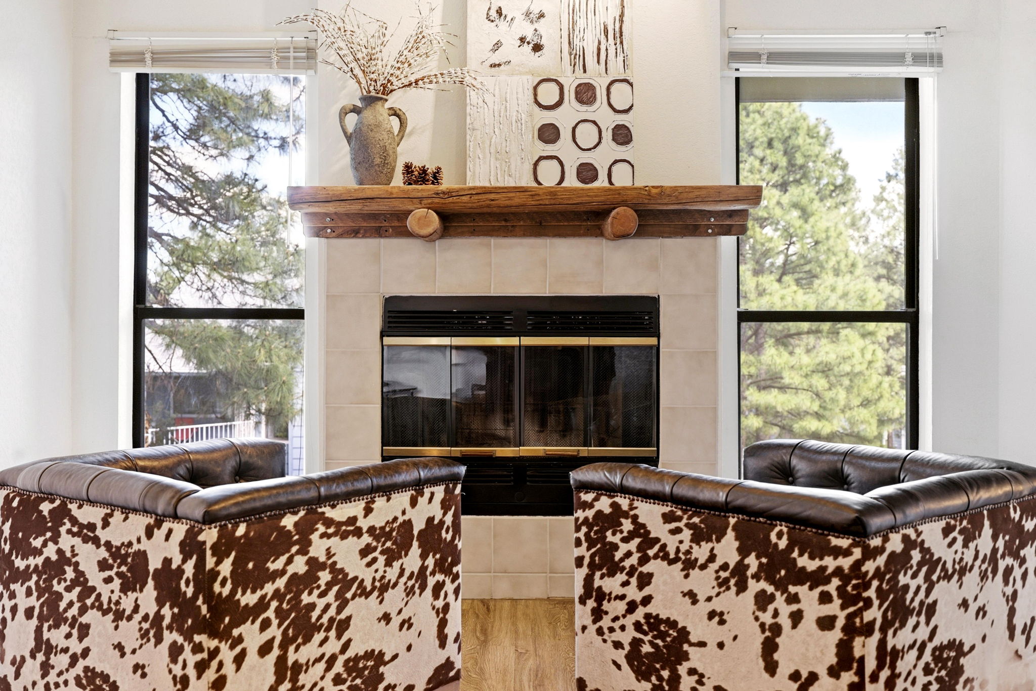 Cozy fireplace framed by tall windows with peaceful pine tree views.