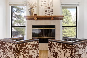 Cozy fireplace framed by tall windows with peaceful pine tree views.