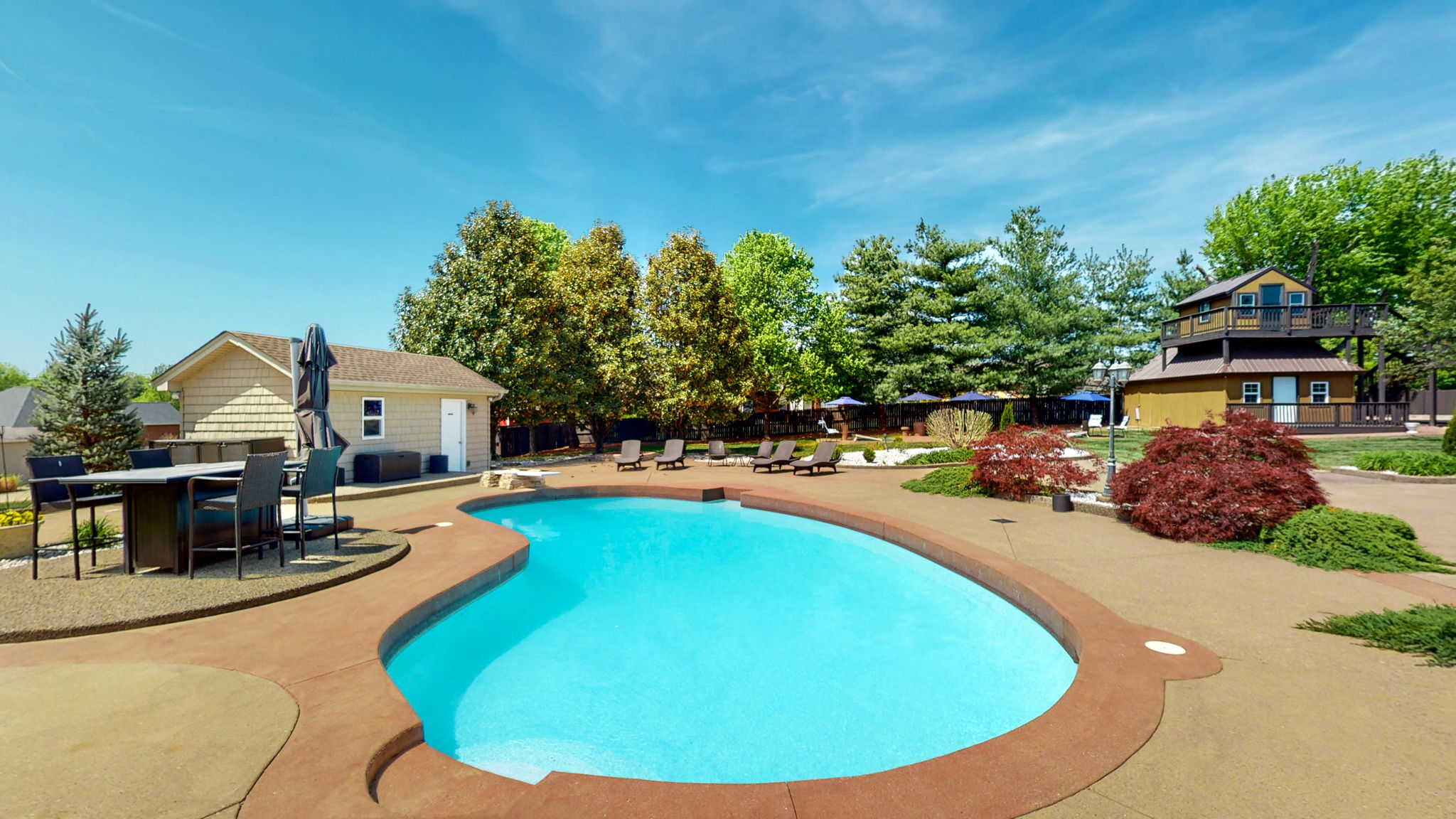 Beyond this saltwater pool, is a paved concrete cornhole court.  You can also see the pool house and the treehouse in proximity to the pool.