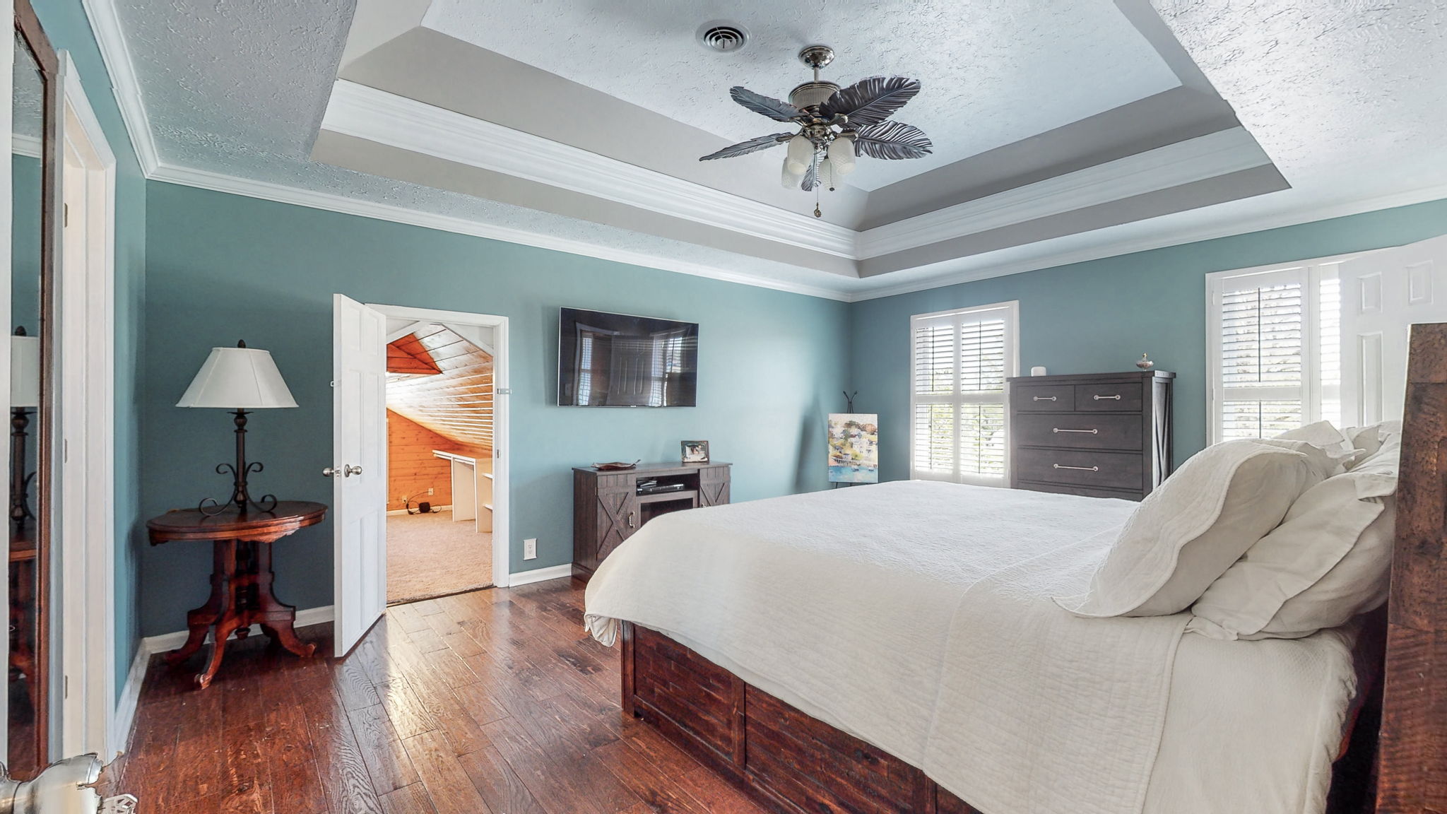 With a beautiful tray ceiling, soothing ceiling fan, and elegant wood floors, this spacious master bedroom is warm and inviting.