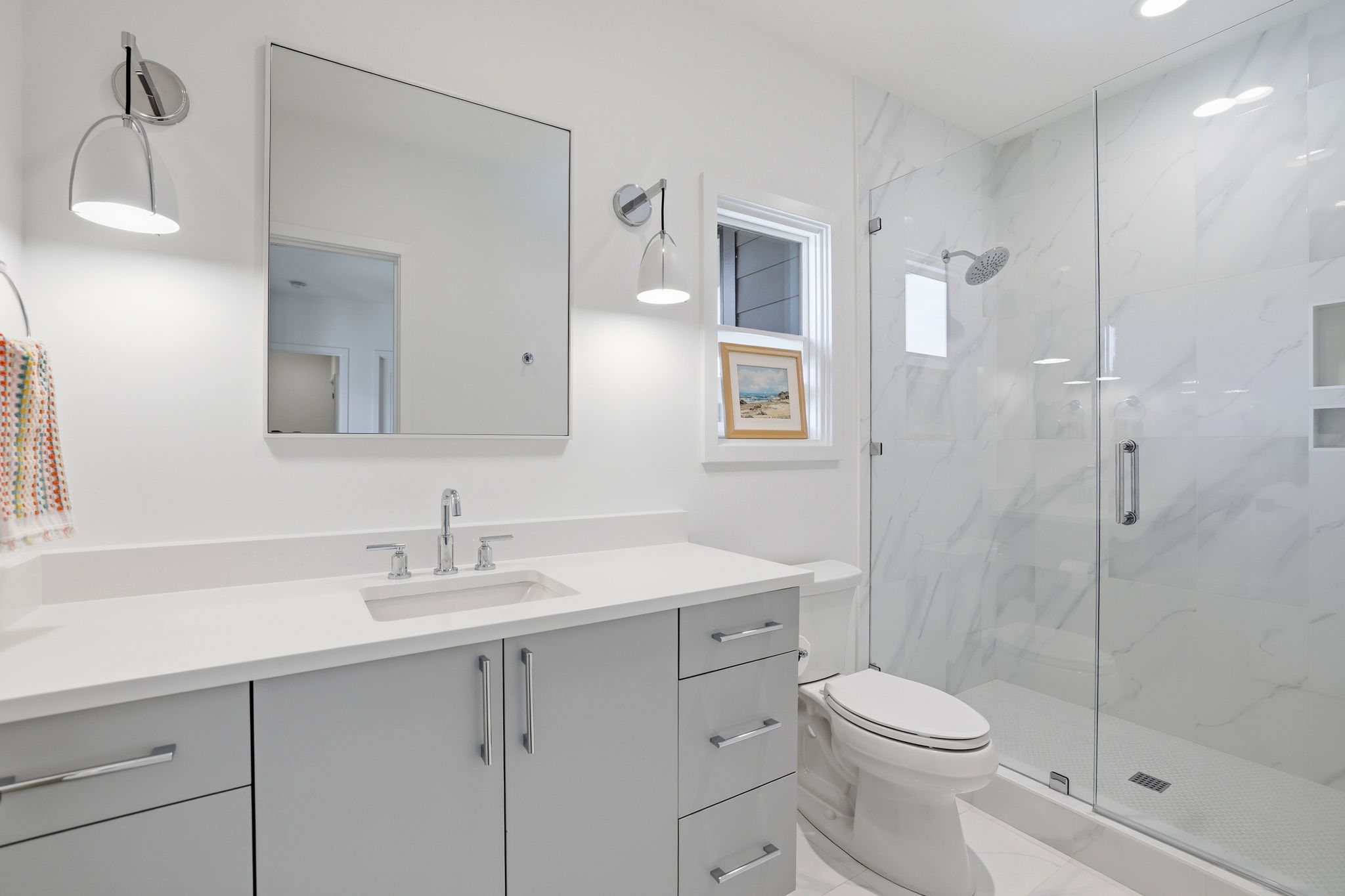 Refined and stylish, this en-suite bath showcases a frameless glass shower and designer light fixtures