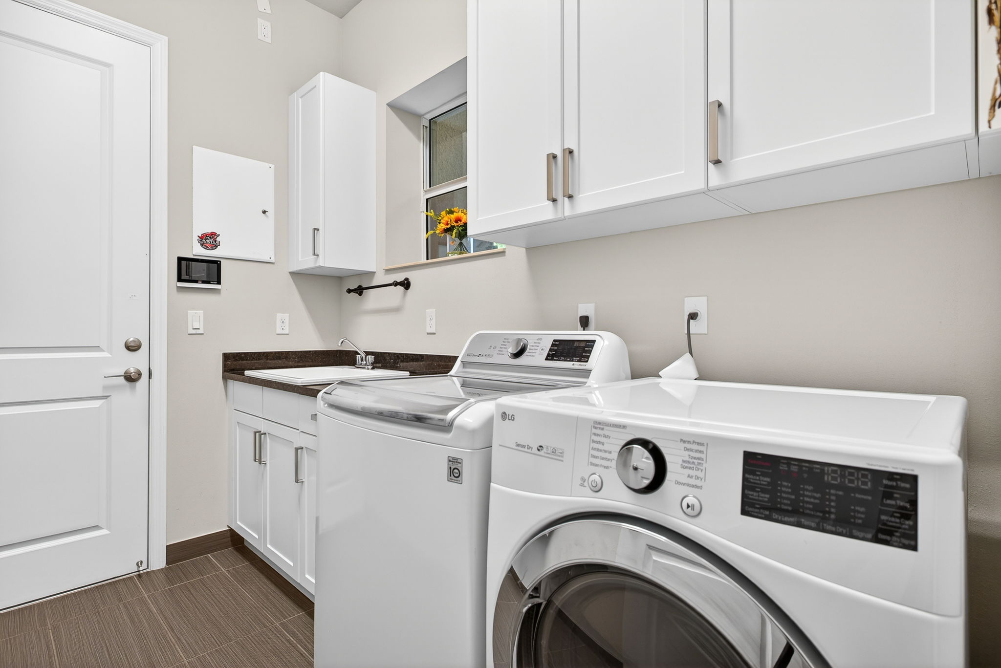 Sink, window, cabinetry galore, and updated washer and gas dryer comprise this laundry room.