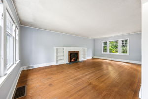 View from the entry of large living room with a fireplace, hardwood floors and lots of windows.