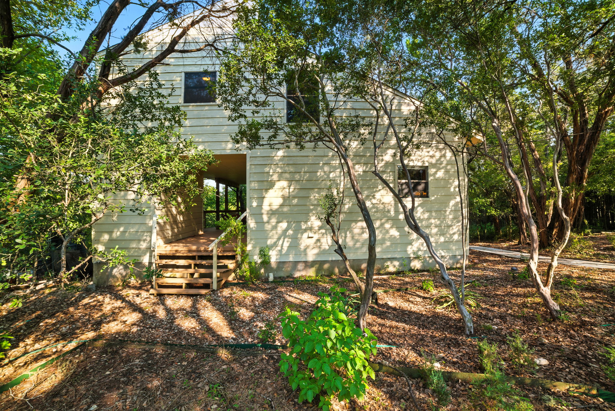 This wide view of the front exterior highlights the natural setting and additional storage space, surrounded by mature trees that frame the home with privacy. The thoughtful layout makes use of the wooded lot while creating a welcoming approach to the property.