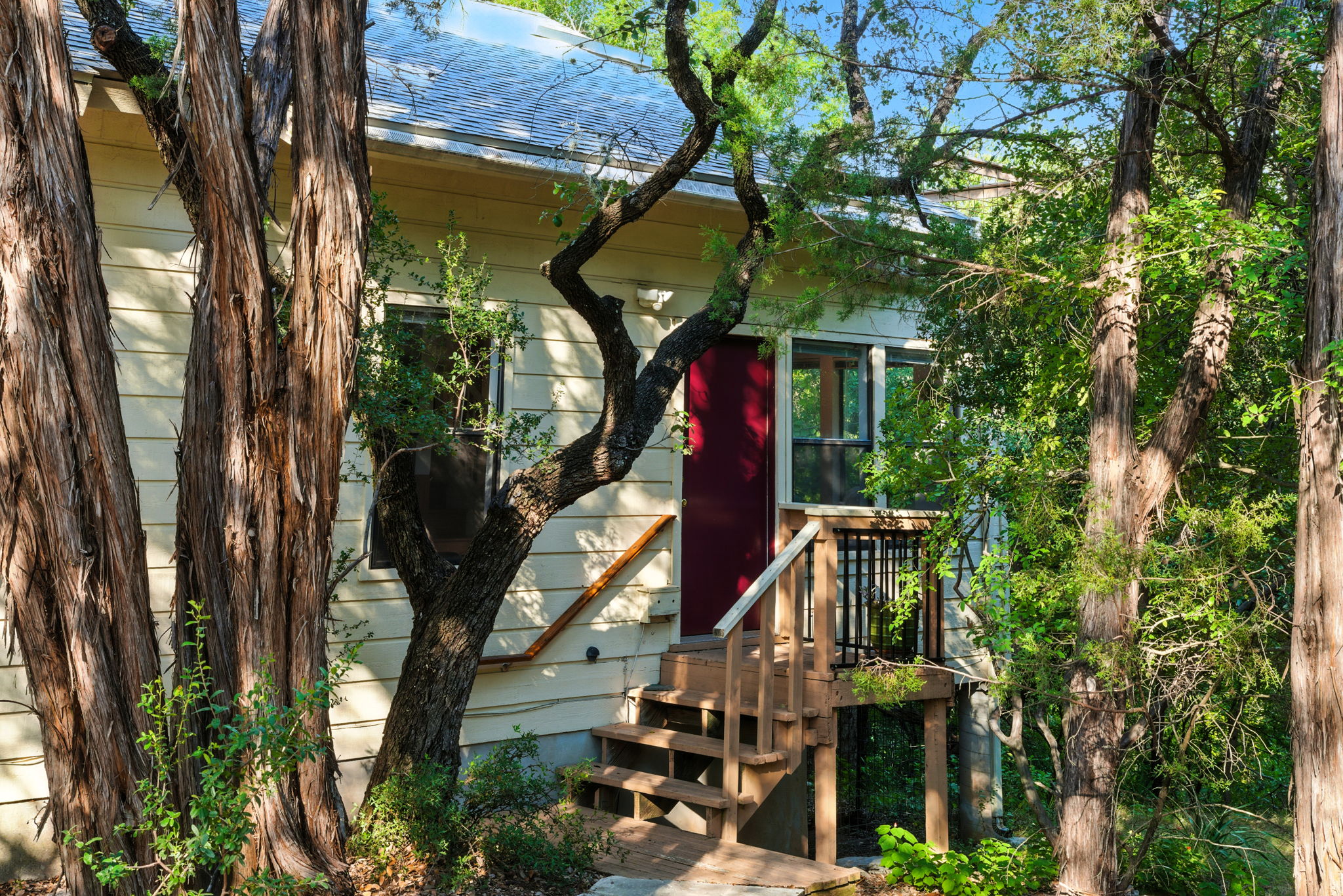 A freshly updated entryway welcomes you with steps leading to a cozy front porch, framed by mature trees for added privacy. The elevated setting creates a natural treehouse vibe while offering a warm first impression of the home.