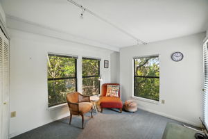 This versatile upstairs bedroom is currently styled as a sitting room, offering a cozy retreat surrounded by treetop views. Generous windows bring in natural light, making the space equally suited for use as a guest room, office, or relaxation area.