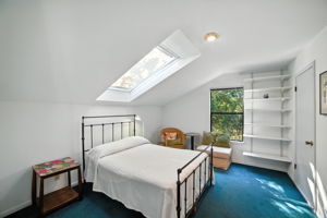 This upstairs bedroom feels bright and airy thanks to a large skylight and a window overlooking the trees. Built-in shelving adds functionality, making the space ideal as a bedroom, guest room, or study.