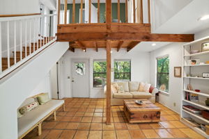 From the entryway, the home opens into a light-filled living room with rustic tile floors and warm wood accents. Large windows showcase treetop views, while the flexible layout flows naturally to the back patio and includes a conveniently located bathroom near the rear entrance—making the space ideal for both everyday living and entertaining.