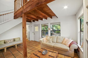 From the back door, the living room opens up with walls of windows that frame the surrounding treetops, filling the space with natural light. Exposed wood beams and tile floors add rustic charm, while the layout creates a cozy gathering space with seamless indoor-outdoor connection.